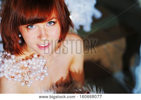 Portrait of beautiful smiling woman with red-brown hair with a pearl necklace on the naked shoulders of new year's eve on blurred background close up