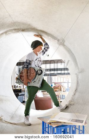 Young lady is holding a gramophone in a concrete drain like posing she is moving her legs and hands in the tube