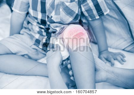 Child injured. Mother bandaging son's knee. Human health care and medicine concept. Doctor makes bandage on knee patient. Photo with color increase blue skin and red spot indicating location of pain.