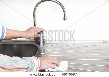 Houseproud woman cleaning a stainless steel sink in her kitchen with a disposable tissue selective focus closeup