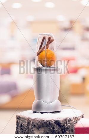 Close view of a silver blender with an orange and cinnamon sticks on a snowy log Christmas gift.