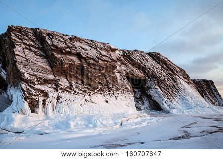Snow-covered rock with grotto on sky background