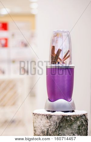 Close view of a blender with cinnamon sticks on a snowy log Christmas gift.