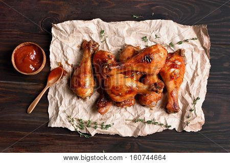 Grilled chicken drumstick on paper over wooden background top view
