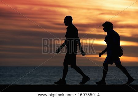 Seniors walking brisk walk along the shore at sunset