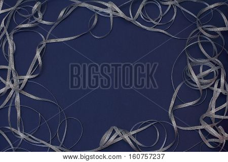 Frame with silver ribbon scrollwork. Christmas/New Year decorations. Dark blue background, top view, flat lay, copy space