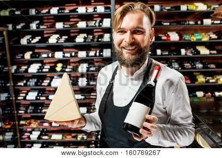 Portrait of a sommelier in uniform with parmegiano cheese and bottle of wine at the restaurant or supermarket. Choosing wine according to the type of cheese. Bottle with empty label to copy paste