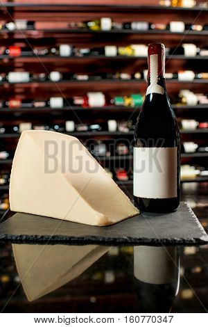 A bottle of wine with a piece of parmegiano cheese on the black board in supermarket or restaurant . Bottle with empty label to copy paste