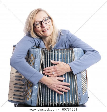 blond woman in blue with glasses holds accordeon and smiles in studio with white background