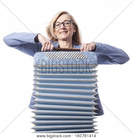 blond woman in blue with glasses holds accordeon and smiles in studio with white background