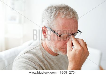 healthcare, pain, stress, age and people concept - senior man suffering from headache at home