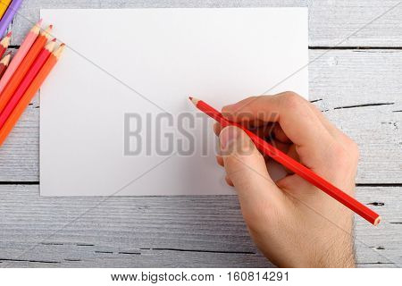 drawing with colored pencils right hand on white paper on white wooden background copy space for text top view.