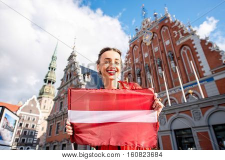 Portrait of a young female tourist with latvian flag on the main old town square in Riga. Woman having great vacations in Latvia