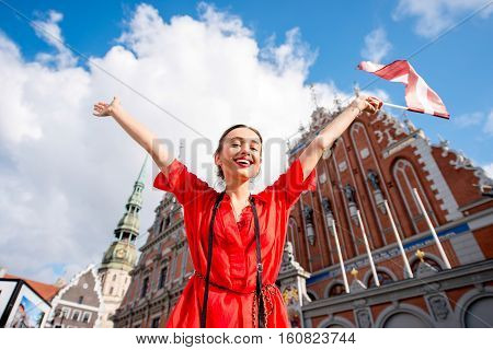 Portrait of a young female tourist with latvian flag on the main old town square in Riga. Woman having great vacations in Latvia
