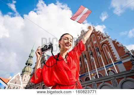 Portrait of a young female tourist with latvian flag on the main old town square in Riga. Woman having great vacations in Latvia