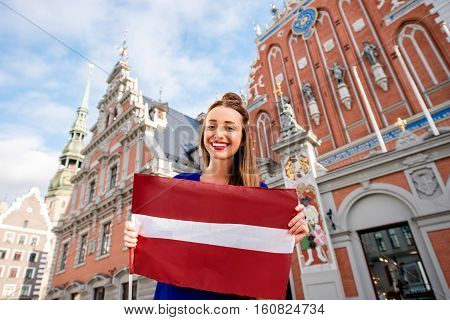 Portrait of a young female tourist with latvian flag on the main old town square in Riga. Woman having great vacations in Latvia