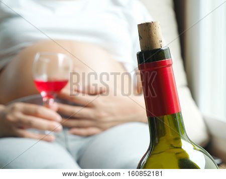 Wine bottle with background of pregnant woman with glass of wine in hand