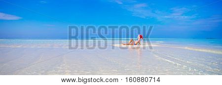 Little cute girl in Santa hat on white beach during vacation