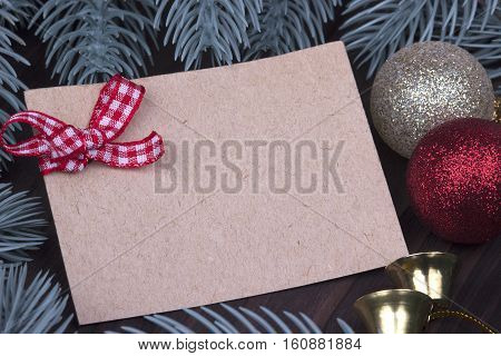 Christmas Xmas New Year Holiday greeting card concept with empty sheet of cardboard Christmas red and golden balls bell bow ribbon fir branches on dark wooden background space for text