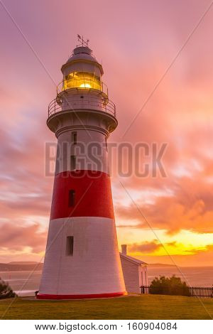 The Low Head Lighthouse North from Georgetown in Tasmania illuminated just before sunset. On the base of the tower are the keepers quarters; view on the background overlooks the Tamar river with its West bank in the distance.