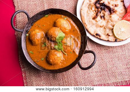 Freshly cooked spicy potato curry in frying pan or Hot and spicy Dum aloo served with tandoori roti or naan or indian bread or chapati and green salad, selective focus