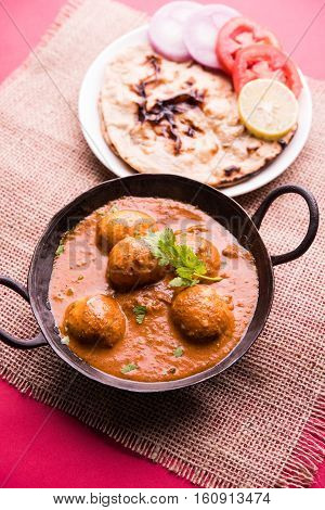 Freshly cooked spicy potato curry in frying pan or Hot and spicy Dum aloo served with tandoori roti or naan or indian bread or chapati and green salad, selective focus