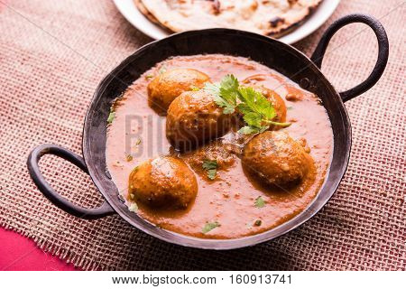 Freshly cooked spicy potato curry in frying pan or Hot and spicy Dum aloo served with tandoori roti or naan or indian bread or chapati and green salad, selective focus