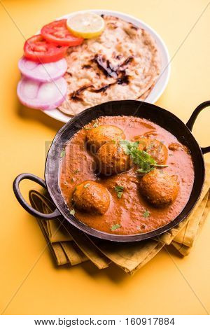 Freshly cooked spicy potato curry in frying pan or Hot and spicy Dum aloo served with tandoori roti or naan or indian bread or chapati and green salad, selective focus