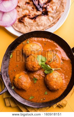 Freshly cooked spicy potato curry in frying pan or Hot and spicy Dum aloo served with tandoori roti or naan or indian bread or chapati and green salad, selective focus