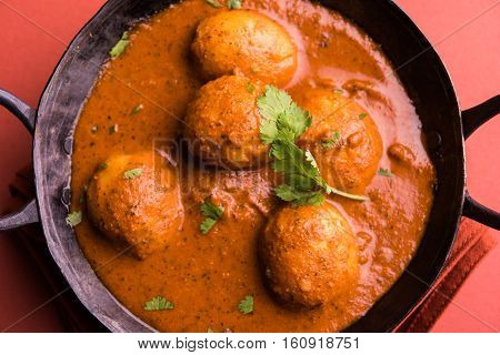 Freshly cooked spicy potato curry in frying pan or Hot and spicy Dum aloo served with tandoori roti or naan or indian bread or chapati and green salad, selective focus