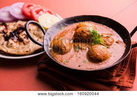 Freshly cooked spicy potato curry in frying pan or Hot and spicy Dum aloo served with tandoori roti or naan or indian bread or chapati and green salad, selective focus