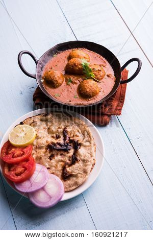 Freshly cooked spicy potato curry in frying pan or Hot and spicy Dum aloo served with tandoori roti or naan or indian bread or chapati and green salad, selective focus