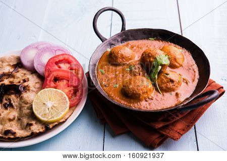 Freshly cooked spicy potato curry in frying pan or Hot and spicy Dum aloo served with tandoori roti or naan or indian bread or chapati and green salad, selective focus