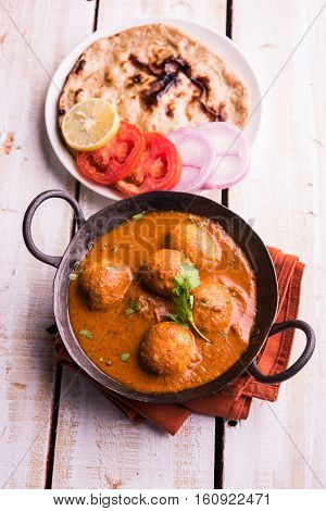 Freshly cooked spicy potato curry in frying pan or Hot and spicy Dum aloo served with tandoori roti or naan or indian bread or chapati and green salad, selective focus