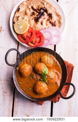 Freshly cooked spicy potato curry in frying pan or Hot and spicy Dum aloo served with tandoori roti or naan or indian bread or chapati and green salad, selective focus