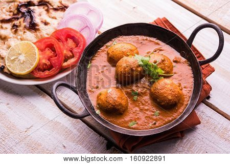 Freshly cooked spicy potato curry in frying pan or Hot and spicy Dum aloo served with tandoori roti or naan or indian bread or chapati and green salad, selective focus
