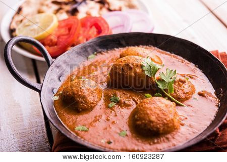 Freshly cooked spicy potato curry in frying pan or Hot and spicy Dum aloo served with tandoori roti or naan or indian bread or chapati and green salad, selective focus