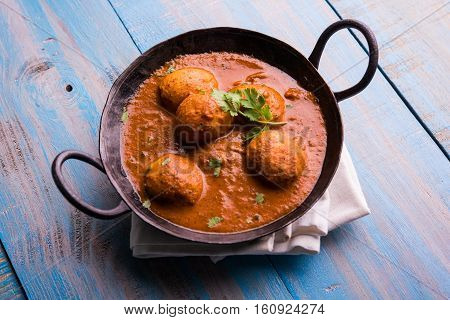 Freshly cooked spicy potato curry in frying pan or Hot and spicy Dum aloo served with tandoori roti or naan or indian bread or chapati and green salad, selective focus