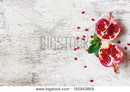 ripe pomegranate divided into two pieces with seeds on white wooden background with copy space. top view