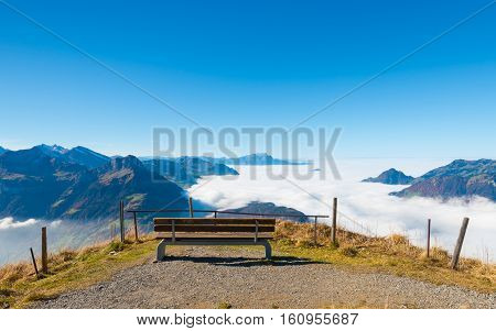 Aerial view. Peak. Bench to rest on the edge. Below clouds and a lake.