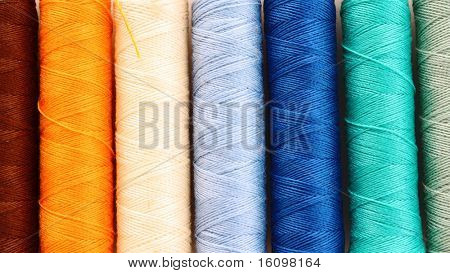 Pile of coloured bobbins of lurex thread isolated on white