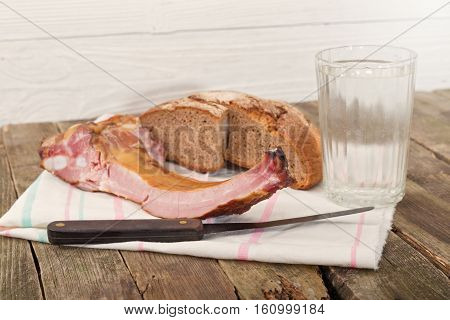 Rye bread ham on edges and a glass of water. On a pure towel bread ham and a knife nearby a glass of water lies. Products on an old wooden table rural style