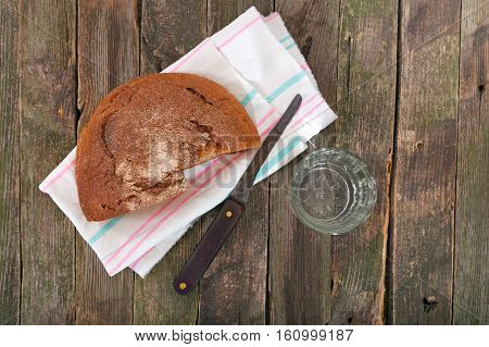 Rye bread and glass of water. On a pure towel bread and a knife nearby a glass of water lies. products on an old wooden table rural style