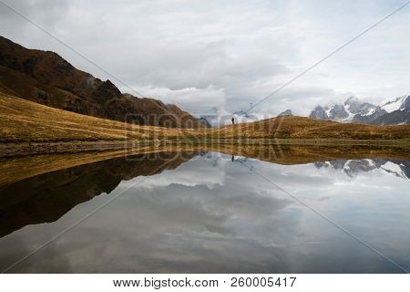 Mountain lake with a mirror reflection of clouds. View of Main Caucasian ridge. Hiker stands on the hill. Koruldi, Samegrelo-zemo svaneti, Georgia