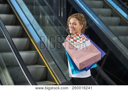 View From Side Of Cheerful Lady With Shopping Bags, Looking At Camera And Laughing In Mall. Attracti
