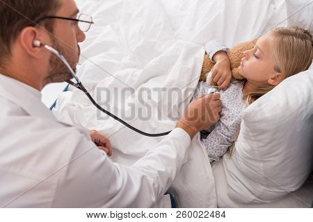 High Angle View Of Pediatrician Litening Childs Breath With Stethoscope While She Lying In Bed