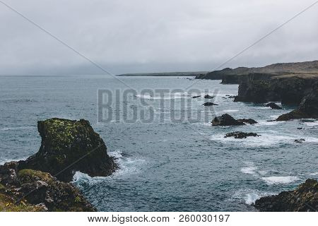 Dramatic Shot Of Rocks And Cliff In Blue Ocean In Arnarstapi, Iceland On Stormy Day