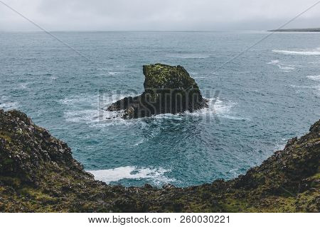 Dramatic Shot Of Rock In Blue Ocean In Arnarstapi, Iceland On Stormy Day