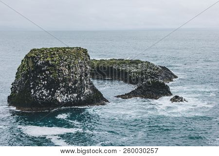 Dramatic Shot Of Rock In Blue Ocean In Arnarstapi, Iceland On Cloudy Day