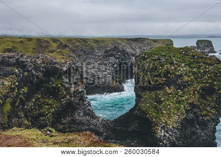 Beautiful Mossy Cliffs In Front Of Blue Ocean In Arnarstapi, Iceland On Cloudy Day